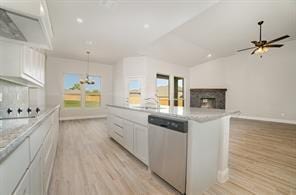 kitchen featuring light wood-style flooring, a fireplace, white cabinetry, and stainless steel dishwasher