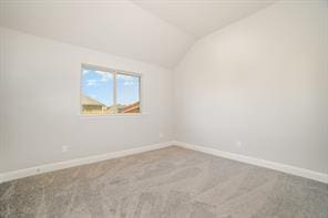 spare room featuring carpet floors, lofted ceiling, and baseboards