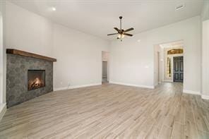 unfurnished living room with light wood-type flooring, a warm lit fireplace, baseboards, and a ceiling fan