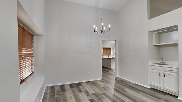 unfurnished dining area featuring baseboards, a towering ceiling, wood finished floors, a sink, and a notable chandelier