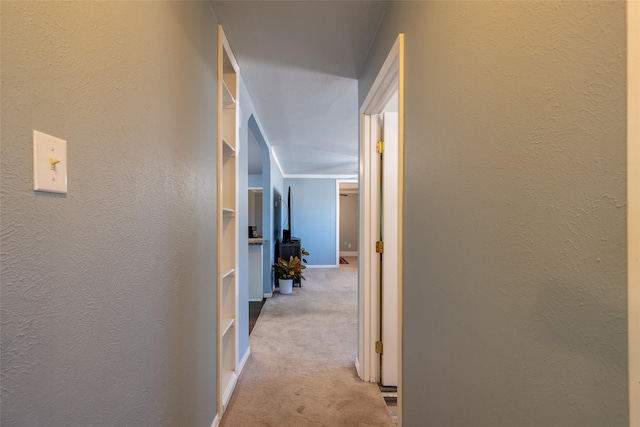 hallway featuring carpet floors, a textured wall, and baseboards