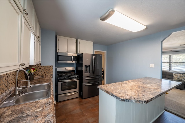 kitchen featuring arched walkways, stainless steel appliances, a sink, white cabinets, and tasteful backsplash