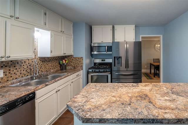 kitchen with appliances with stainless steel finishes, a sink, white cabinetry, and tasteful backsplash