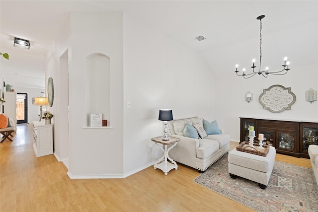 living area with baseboards, visible vents, lofted ceiling, wood finished floors, and an inviting chandelier