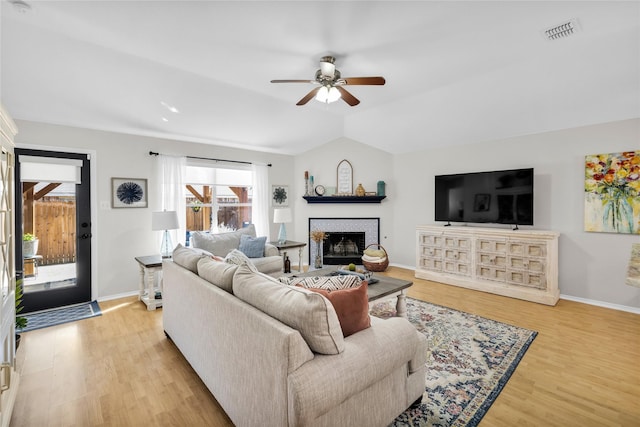 living room with lofted ceiling, visible vents, light wood-style floors, a tile fireplace, and baseboards