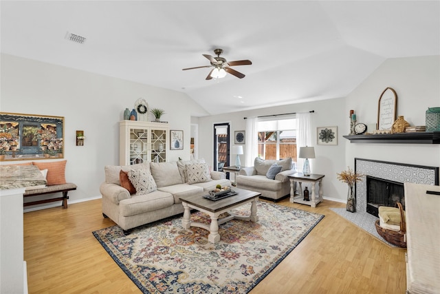 living room with visible vents, a ceiling fan, a tile fireplace, wood finished floors, and vaulted ceiling