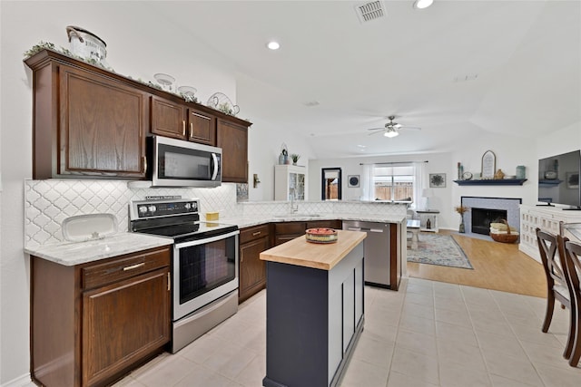 kitchen featuring visible vents, butcher block counters, a fireplace with flush hearth, appliances with stainless steel finishes, and a peninsula