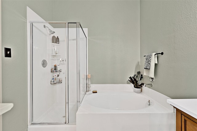 full bath with a textured wall, a stall shower, vanity, and a bath