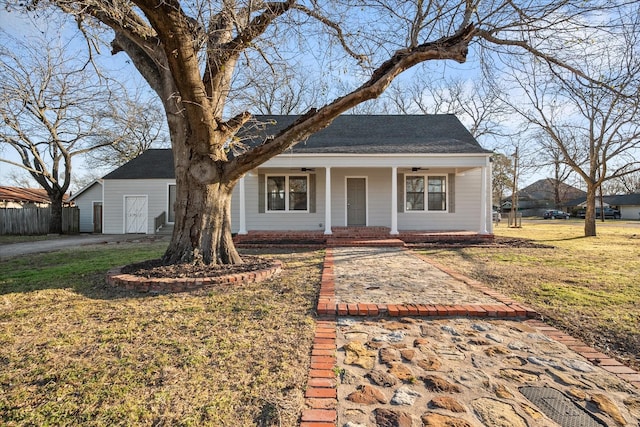 view of front of house with a front yard, covered porch, fence, and an outbuilding