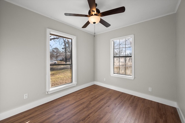 empty room with ornamental molding, dark wood finished floors, plenty of natural light, and baseboards