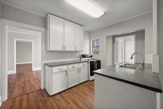 kitchen with dark countertops, gas range oven, white cabinets, and a sink