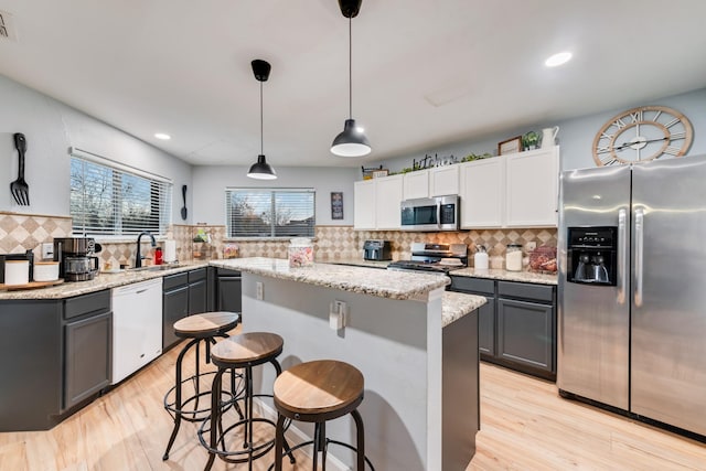 kitchen featuring stainless steel appliances, a kitchen island, a sink, and light wood-style floors