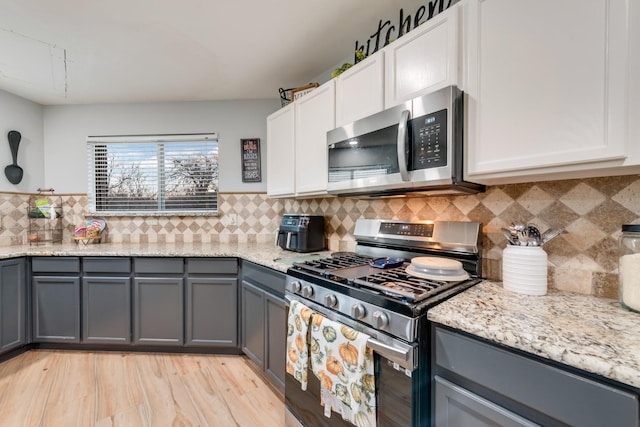 kitchen featuring stainless steel appliances, tasteful backsplash, gray cabinetry, and light stone countertops