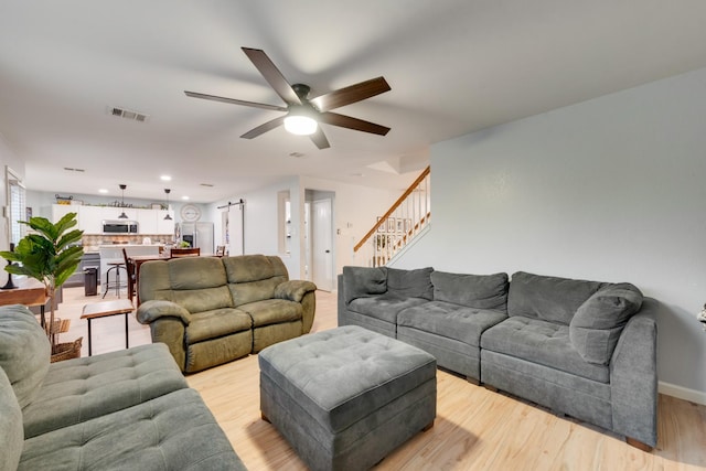 living area featuring baseboards, visible vents, a ceiling fan, stairs, and light wood-type flooring