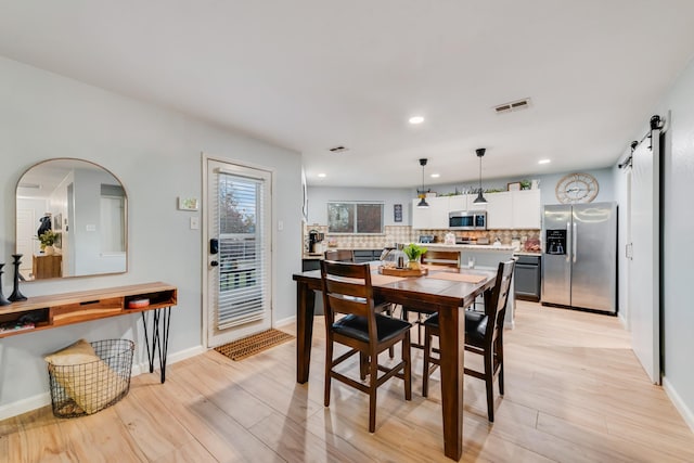 dining area featuring baseboards, visible vents, light wood finished floors, and a barn door