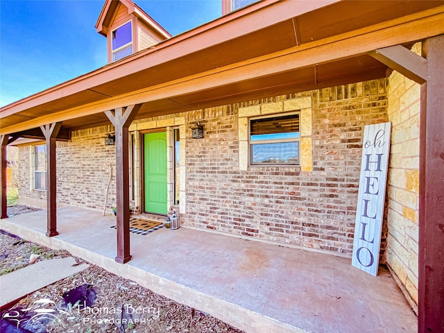 view of exterior entry with brick siding and a porch