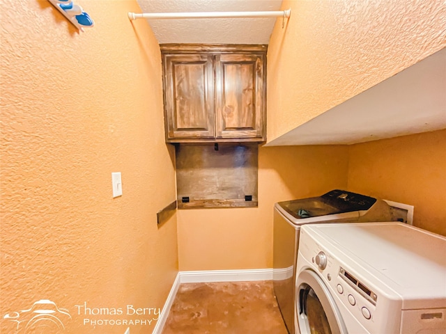 washroom with washing machine and dryer, cabinet space, a textured wall, and baseboards