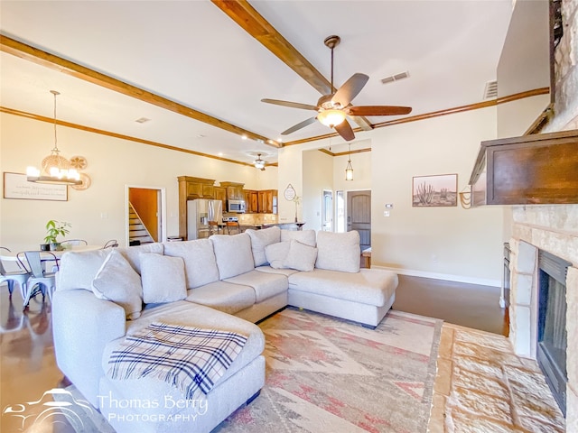 living room featuring beam ceiling, crown molding, a fireplace with raised hearth, visible vents, and ceiling fan with notable chandelier