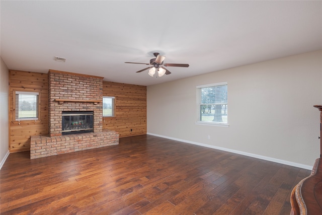 unfurnished living room featuring plenty of natural light, wood-type flooring, a fireplace, and wood walls