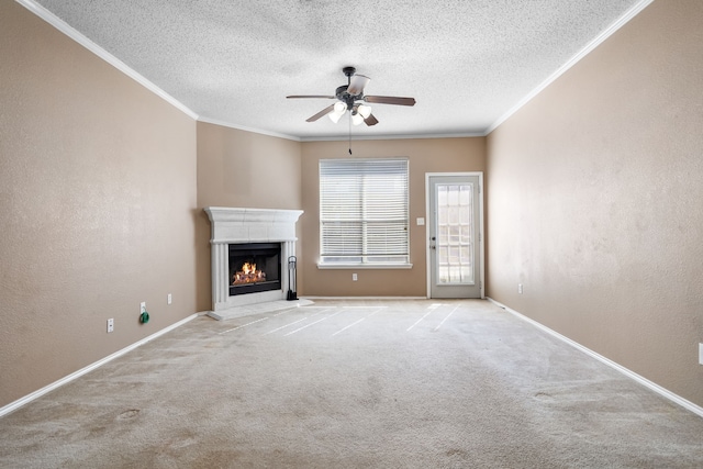 unfurnished living room with a textured wall, a ceiling fan, a lit fireplace, ornamental molding, and carpet