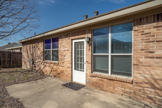 view of exterior entry with brick siding, fence, and a patio