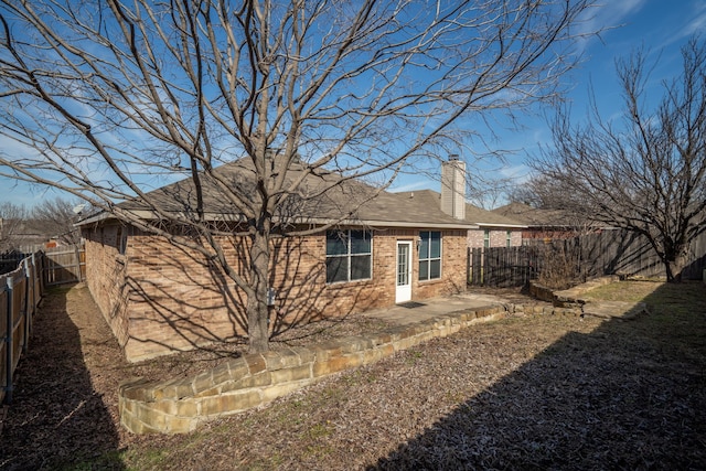 rear view of house featuring a fenced backyard, a chimney, a patio, and brick siding