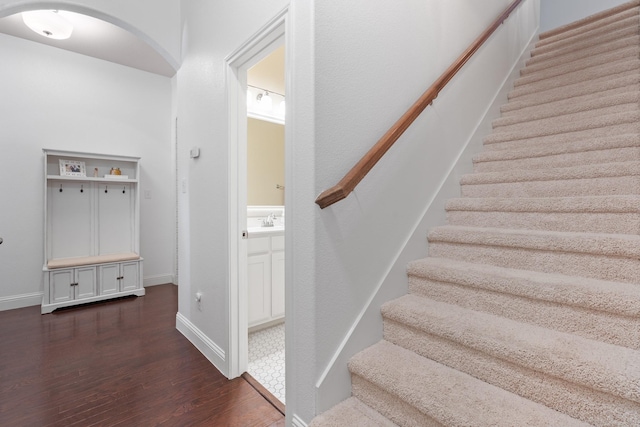 stairway with arched walkways, baseboards, and wood finished floors