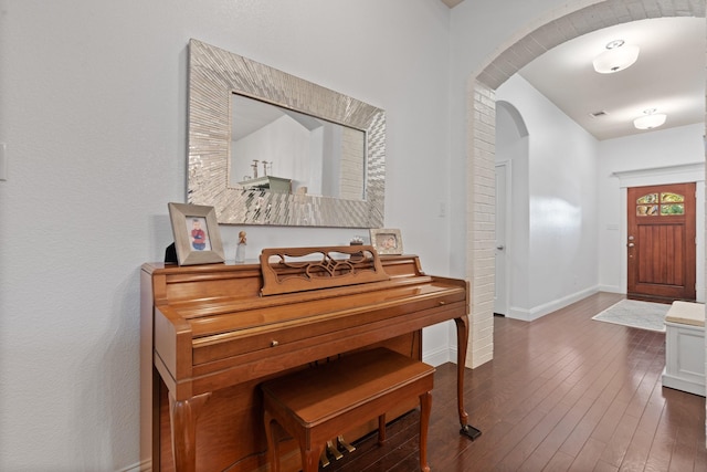 entryway with arched walkways, dark wood-style flooring, and baseboards