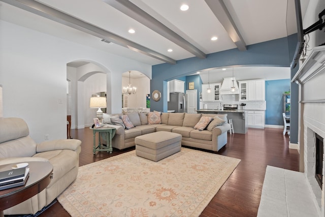 living room featuring a notable chandelier, visible vents, a brick fireplace, beamed ceiling, and dark wood finished floors