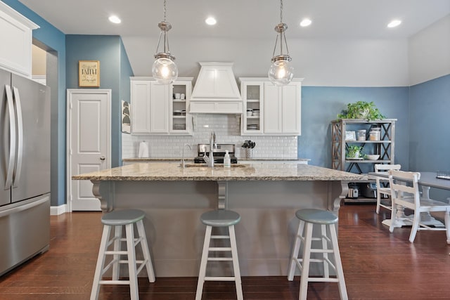 kitchen with light stone counters, a sink, white cabinets, freestanding refrigerator, and dark wood finished floors