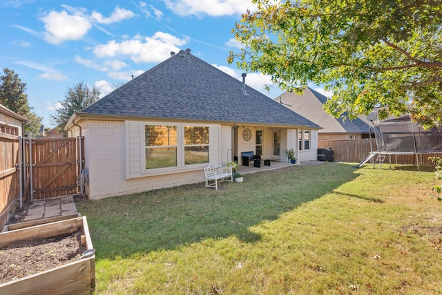 back of property with a trampoline, a shingled roof, a fenced backyard, a gate, and a garden