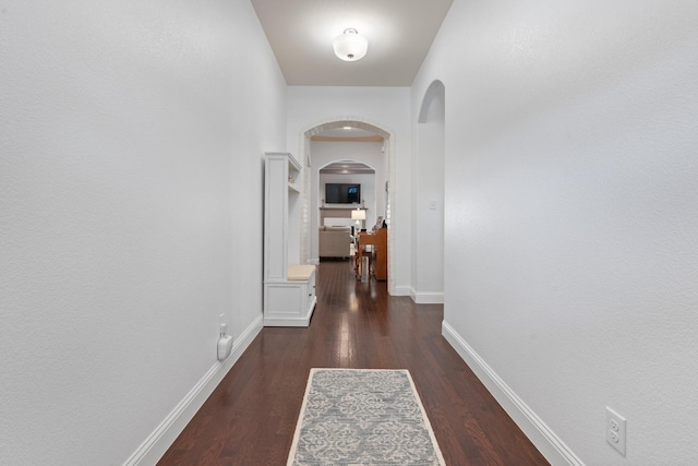 corridor with arched walkways, dark wood-style flooring, and baseboards