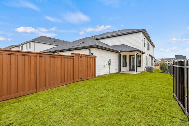 rear view of property with a shingled roof, a lawn, a patio area, central AC, and a fenced backyard