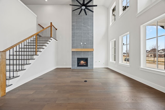 unfurnished living room featuring baseboards, a towering ceiling, a tiled fireplace, and wood finished floors