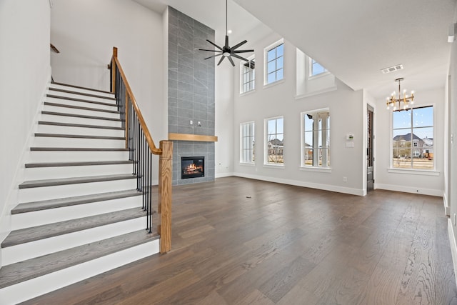 unfurnished living room with visible vents, a tiled fireplace, dark wood-style floors, stairs, and ceiling fan with notable chandelier