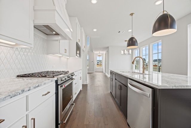 kitchen with stainless steel appliances, tasteful backsplash, custom range hood, white cabinetry, and a sink