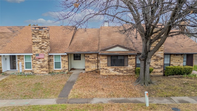 multi unit property with a front yard, roof with shingles, a chimney, and brick siding