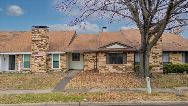 view of front of home featuring roof with shingles, a chimney, and brick siding