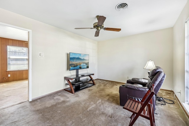 living area featuring wooden walls, baseboards, visible vents, ceiling fan, and carpet flooring