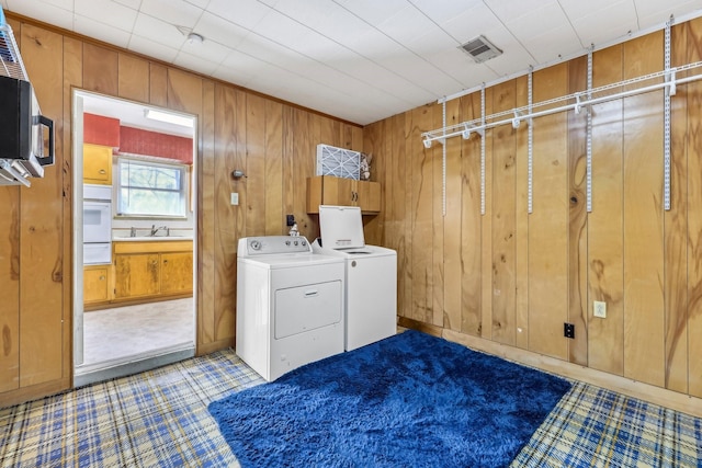 laundry room with a sink, laundry area, wood walls, and washing machine and clothes dryer