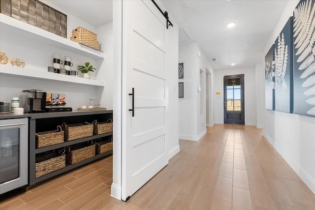 interior space featuring beverage cooler, baseboards, a bar, light wood-style floors, and a barn door