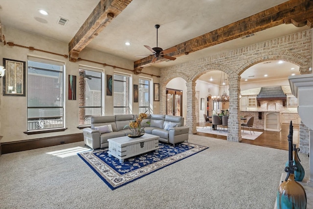 carpeted living room featuring arched walkways, visible vents, ceiling fan, beamed ceiling, and ornate columns