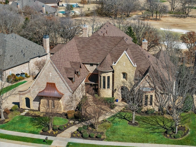 french provincial home with stone siding, a shingled roof, a chimney, and a front yard