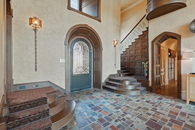 foyer featuring brick floor, a high ceiling, arched walkways, and crown molding