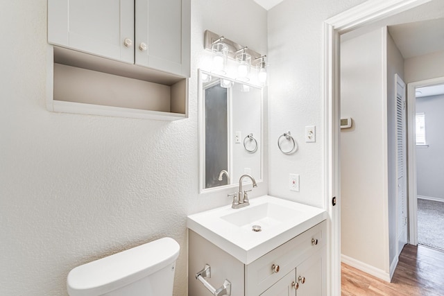 half bath featuring baseboards, a textured wall, toilet, wood finished floors, and vanity