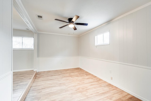 empty room with a wealth of natural light, a ceiling fan, visible vents, and wood finished floors