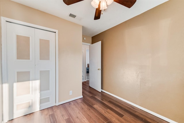 unfurnished bedroom with baseboards, visible vents, ceiling fan, wood finished floors, and a closet