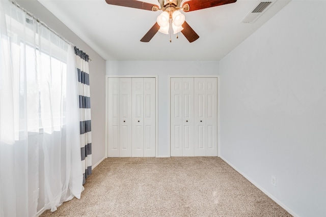 unfurnished bedroom featuring ceiling fan, visible vents, multiple closets, and light colored carpet