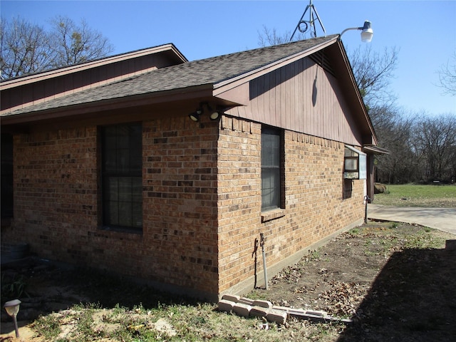 view of side of home with brick siding and roof with shingles