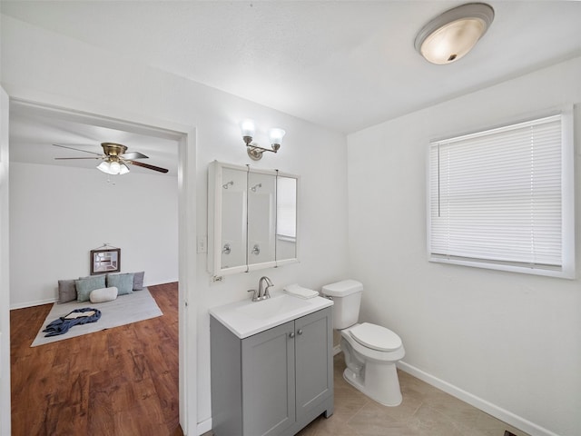 bathroom with baseboards, toilet, ceiling fan, wood finished floors, and vanity